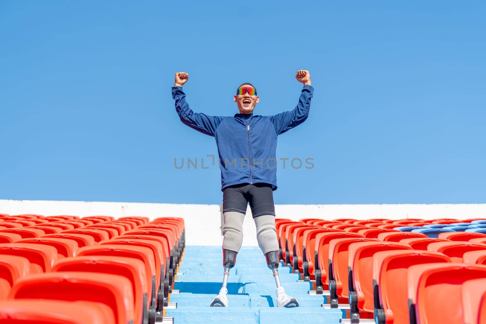 Close up sport man athlete prosthesis legs stand on stairs with action of happy and celebration on amphitheater in the stadium with day light.