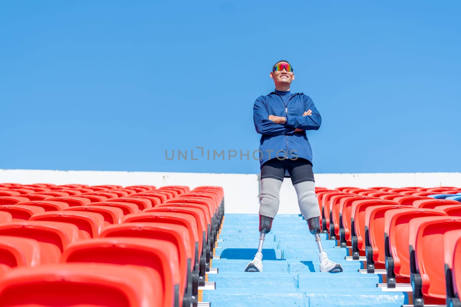 Sport man athlete prosthesis legs stand with arm crossed on stairs with happiness on amphitheater in the stadium with day light.