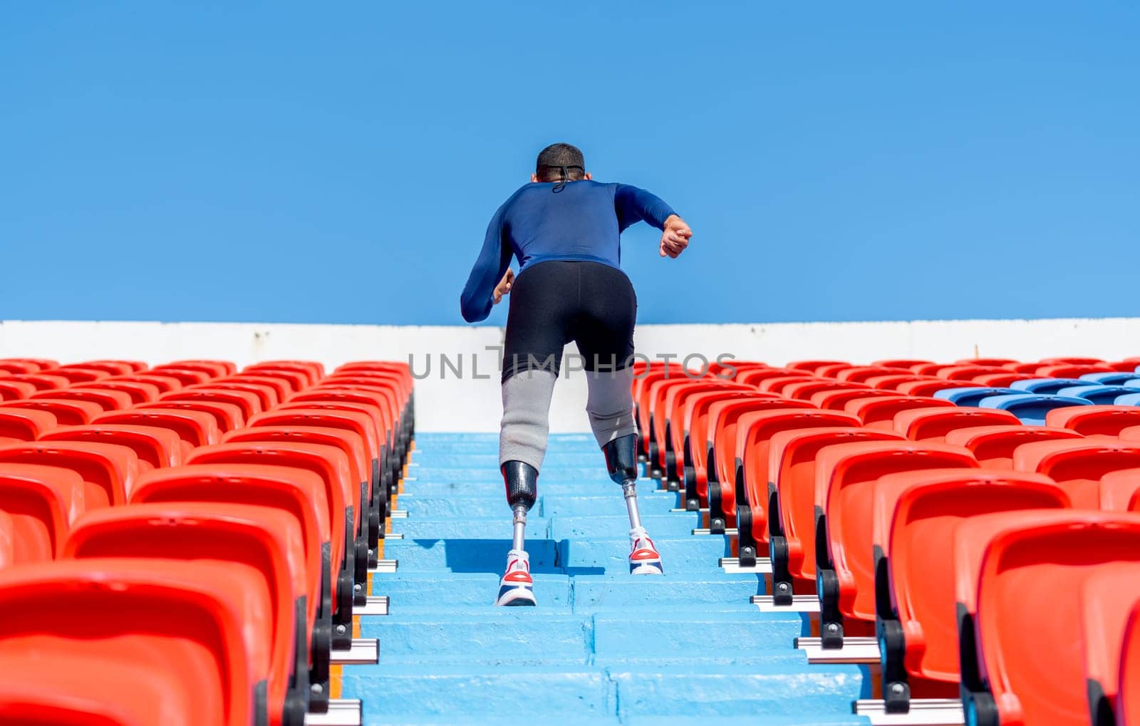 Back of sport man athlete prosthesis legs walk up on stairs of amphitheater in the stadium with day light.