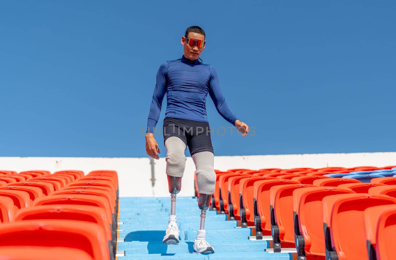 Sport man athlete prosthesis legs walk down on stairs of amphitheater in the stadium with day light.