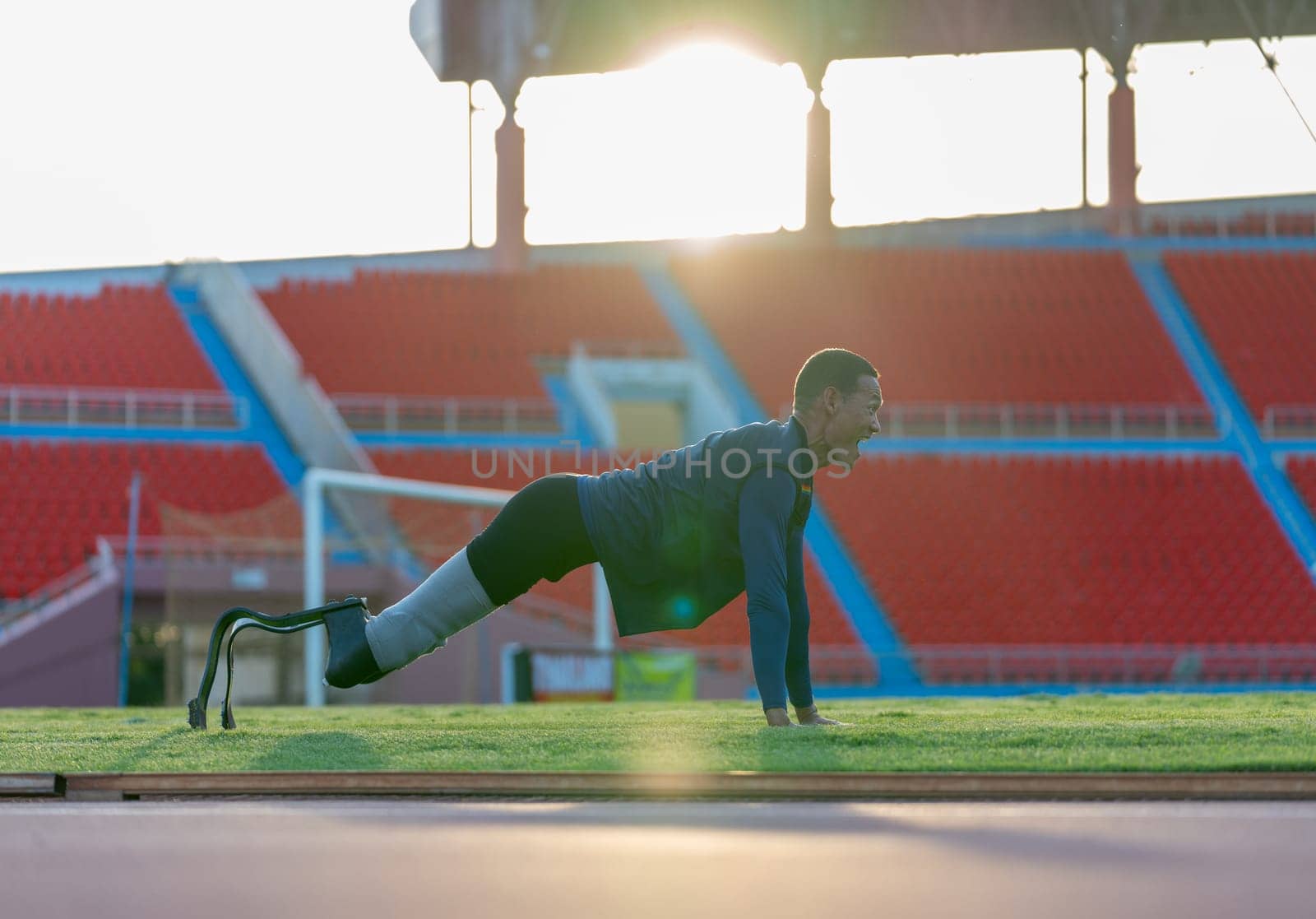 Side view of sport man athlete with a prosthesis on his leg lie down and action of push-ups also look forward to warm up before exercise at the stadium.