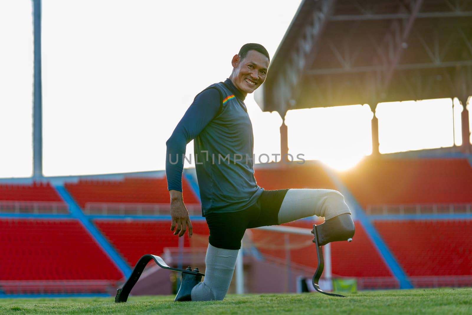 Close up side view sport man athlete prosthesis legs stay in the position of stretching also look at camera in the stadium with soft light of evening.