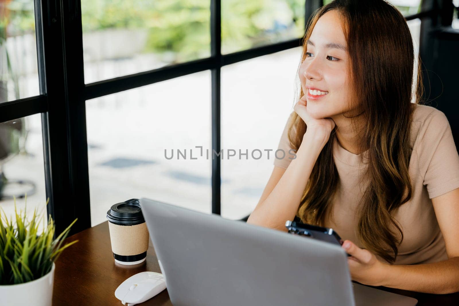 Happy lifestyle female smiling using smartphone in coffee shop, young business woman working with laptop computer she holding smart mobile phone at cefa for texting messages