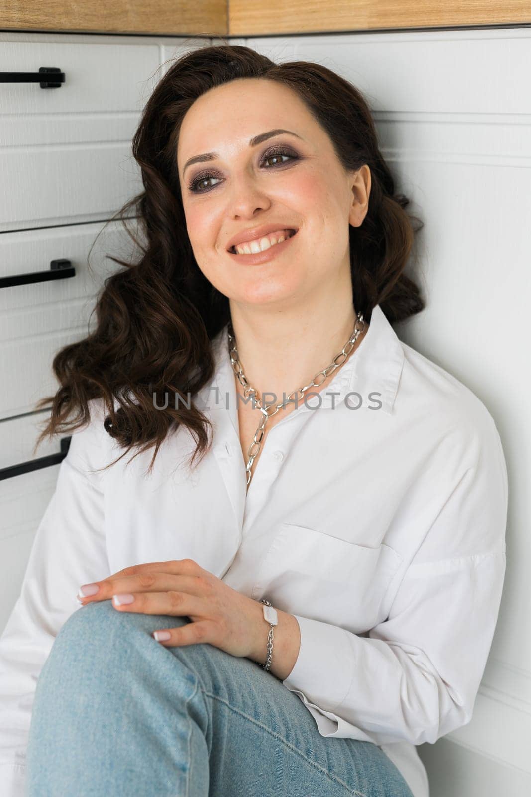 Pretty European emotional woman in a white men's shirt sitting on floor in kitchen. Early morning and smiles when the sun rises. Relaxing and comfortable day.