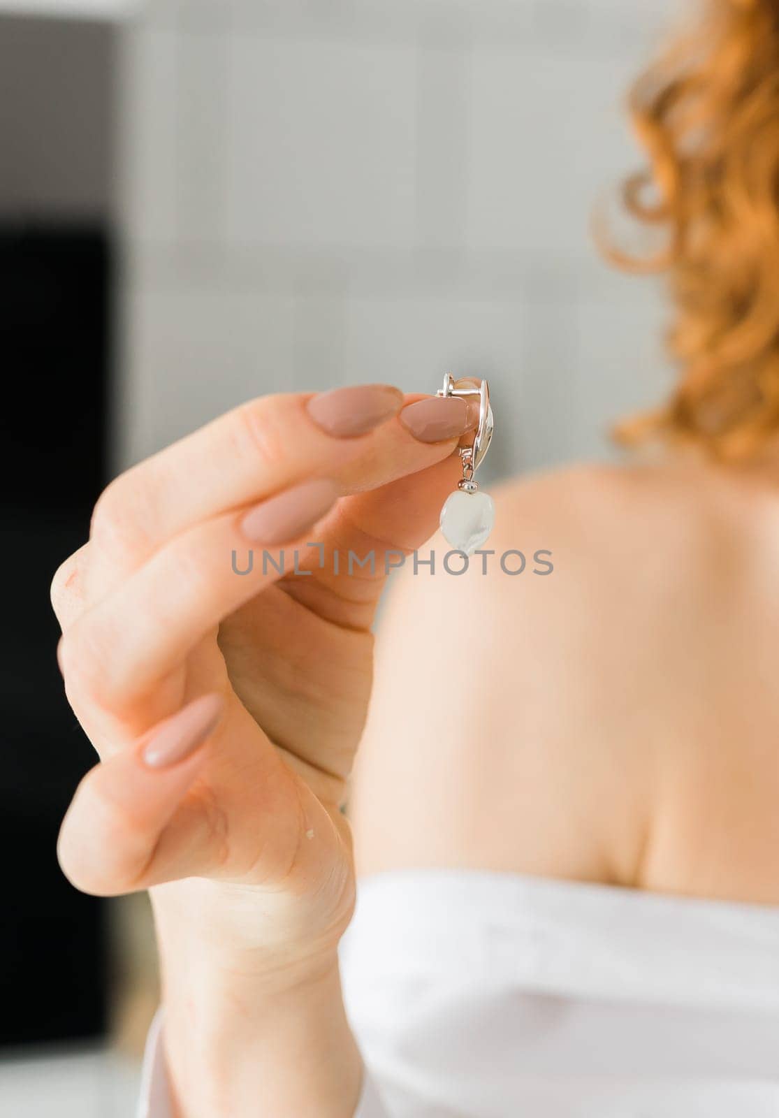 Earring heart shape in female hands. Wedding stylish accessory bride. Elegant bride holding silver earrings. Hands with jewelry. Close up