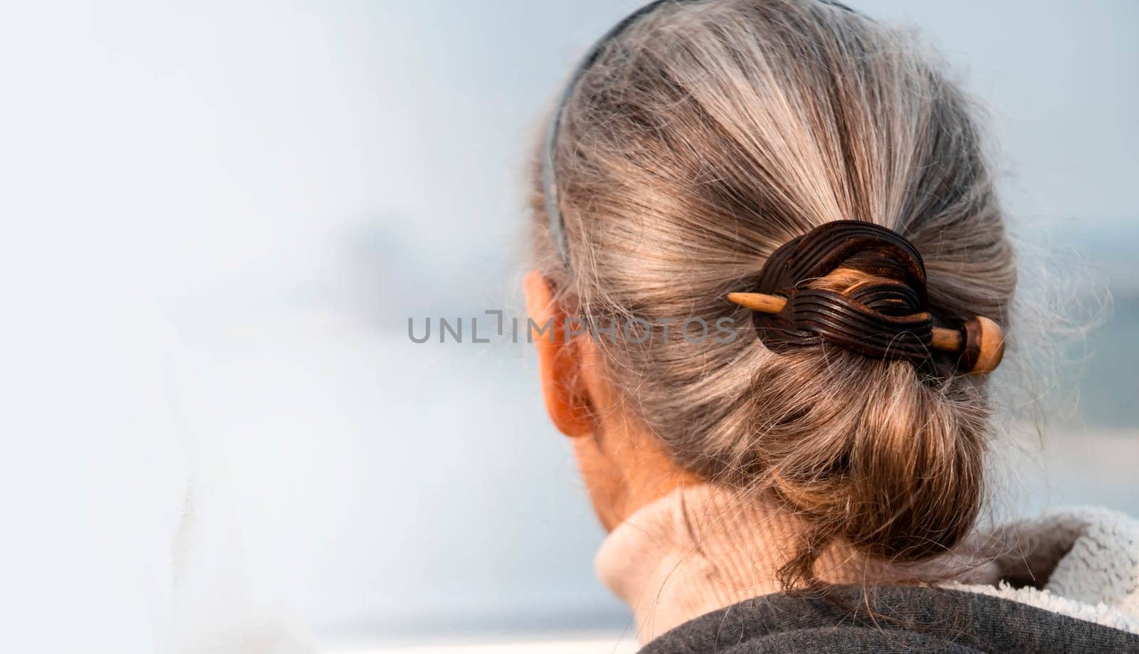 A woman with beautifully styled gray hair, fastened with a hairpin, looks forward, an elderly lady takes care of the health and beauty of her hair and accepts on her natural color.