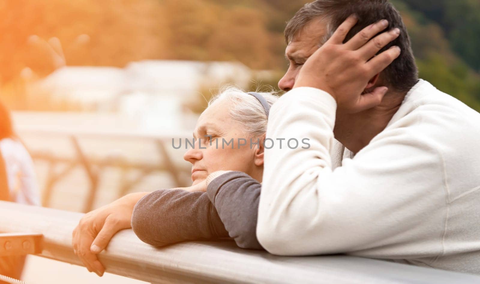 Elderly man and woman are leaning on the railing of the bridge, talking and looking at the city landscape, the old married couple happily spends together, taking care and supporting each other.