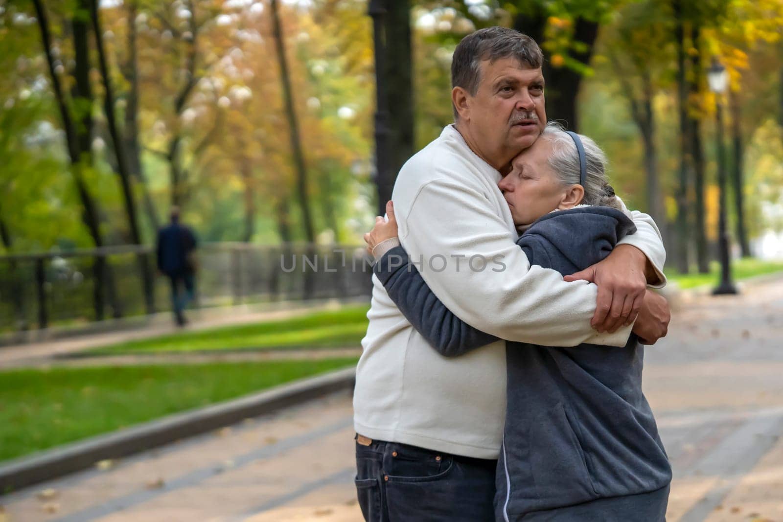 An elderly couple hugs in a park on a walk, a husband hugs his wife tightly and tenderly, supports her during her treatment against disease, a caring man and woman help each other in difficult times.