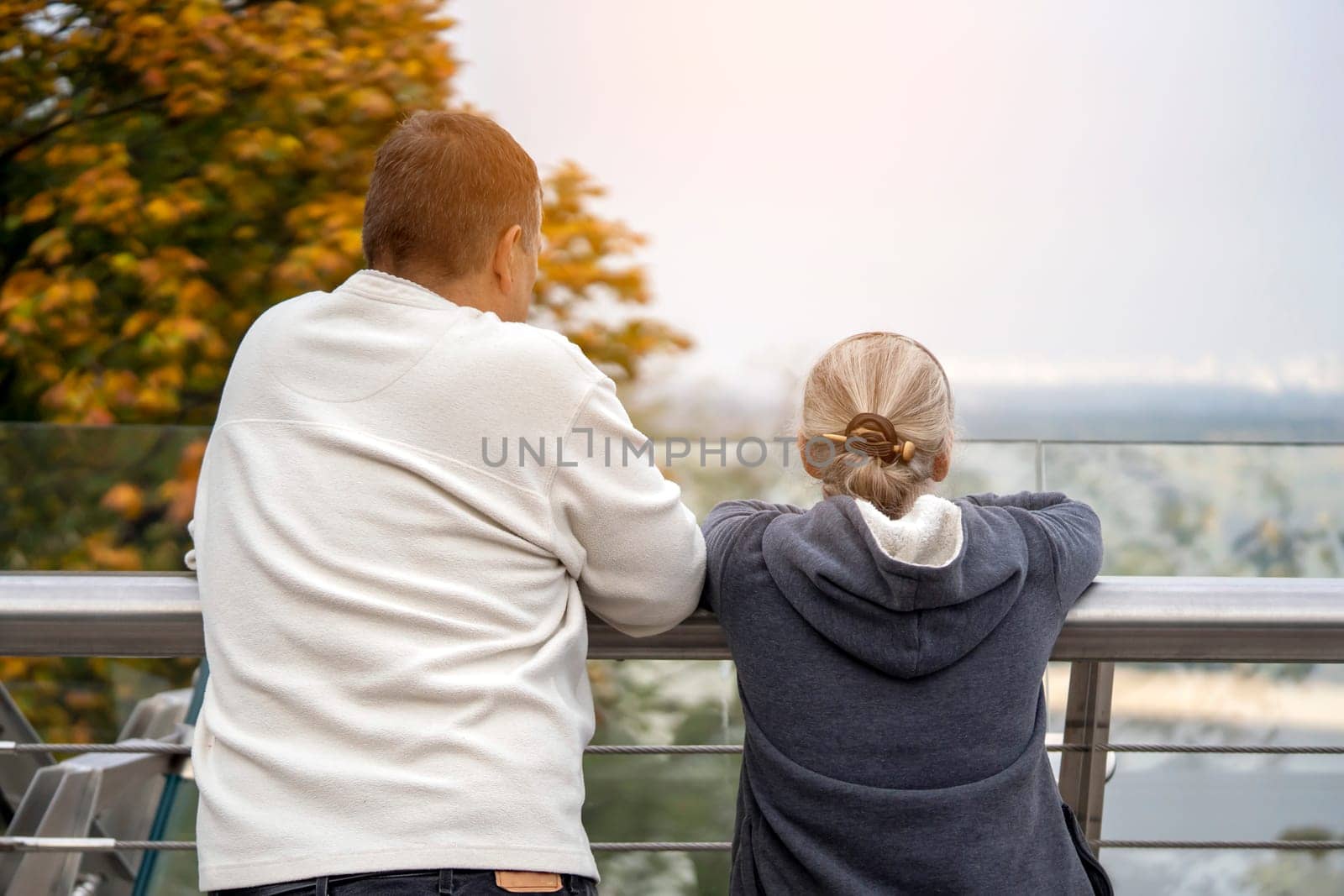 A man and a woman are walking in the park and talking, looking at a beautiful city view - a panorama. Husband and wife aged happily spend time together and support each other.