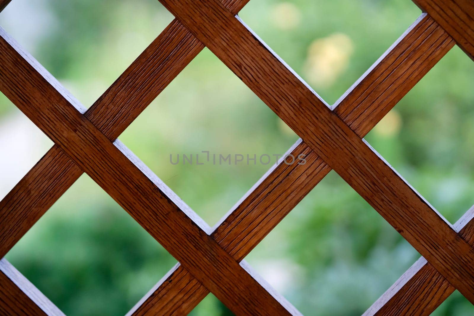 A beautiful background with a wooden lattice, a square grid, a decorative fence on a balcony or terrace against the backdrop of a summer garden, an outdoor fence with a square, rhombic pattern.