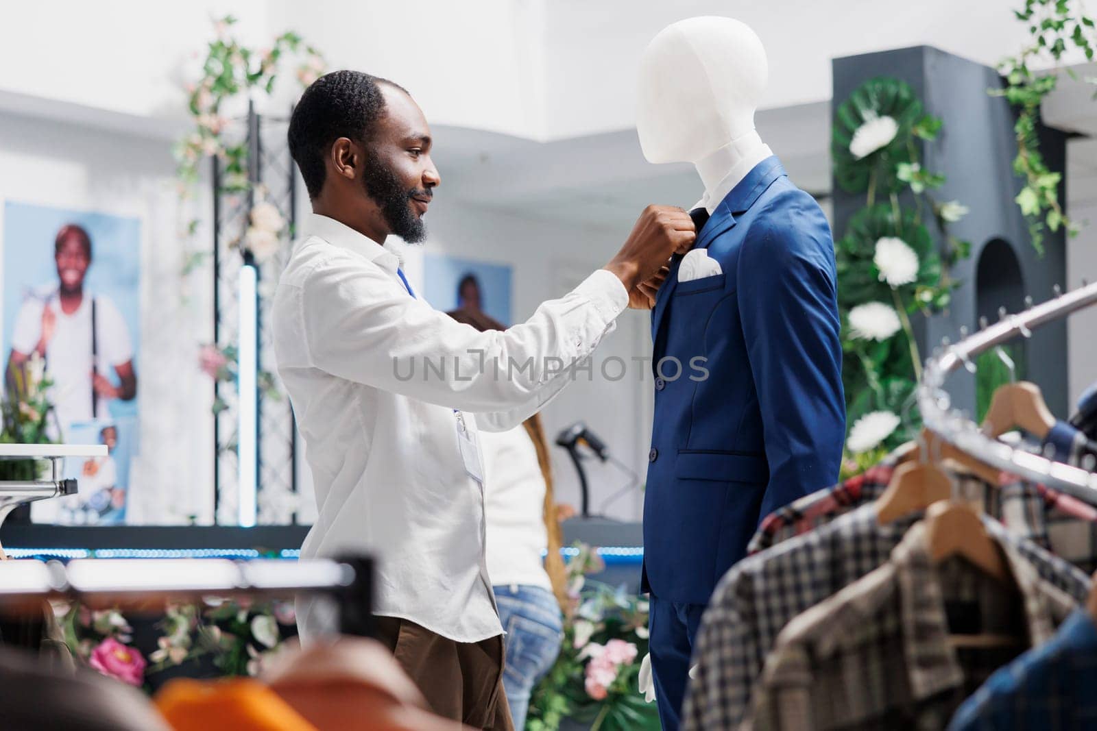 Store worker fixing tie on mannequin wearing formal suit by DCStudio