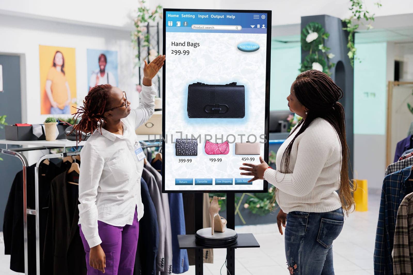 Woman employee showing clothes to client in front of self service checkout kiosk, advising to purchase fashion items in clothing store. Young client talking to assistant about merchandise on board.