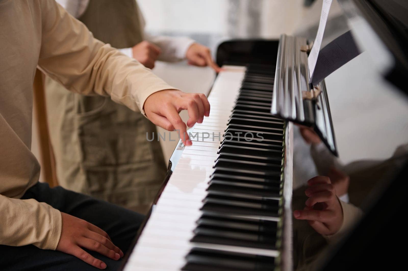 Details on children hands touching white and black piano keys while performing a musical composition, playing grand piano indoor