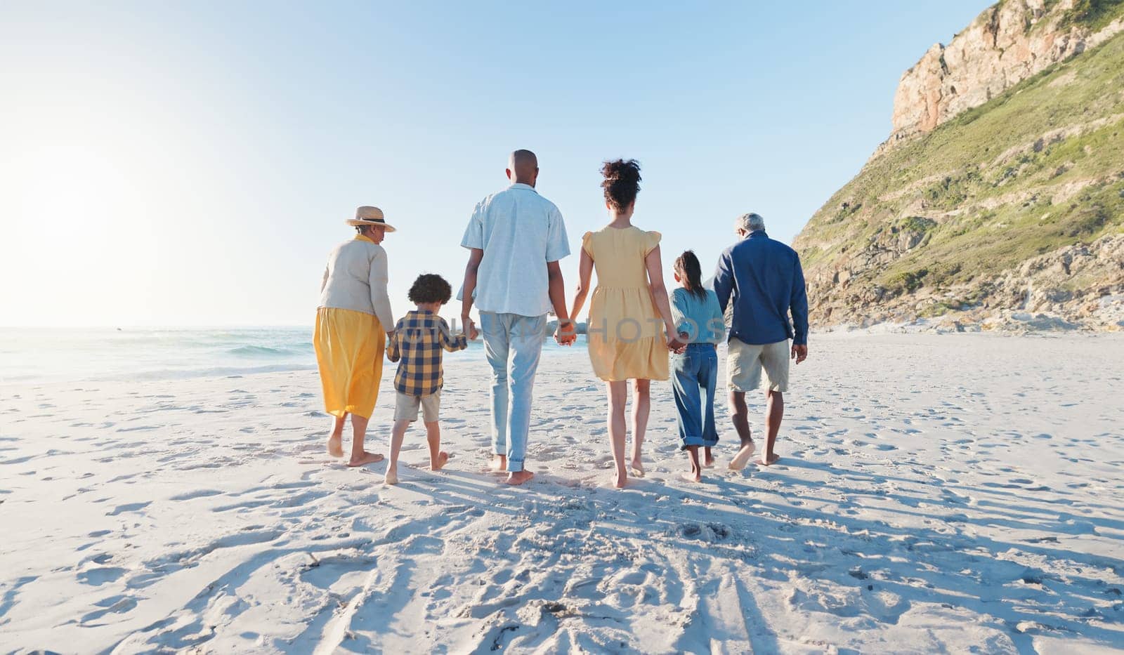 Holding hands, walking and big family at the beach on holiday, adventure or vacation together. Love, travel and children with parents and grandparents on the sand by the ocean or sea on weekend trip