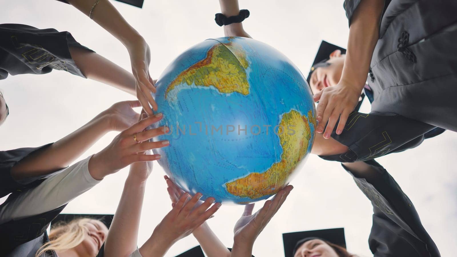 The concept of a world without war. College graduates holding a geographical globe of the world. by DovidPro