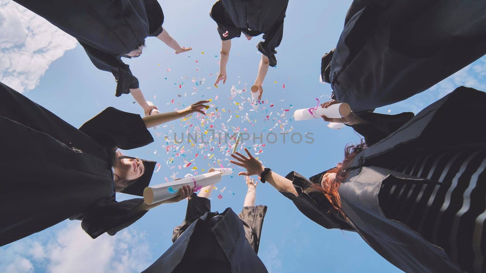 Happy graduates throwing up colorful confetti against the blue summer sky