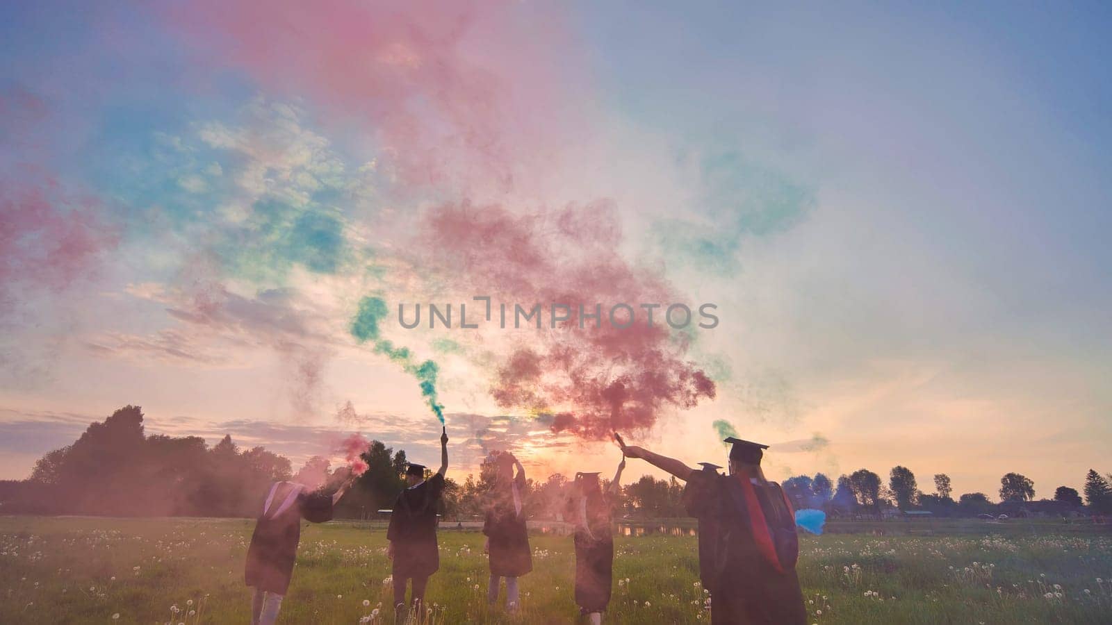 Students graduate with colored smoke walking through the meadow in the evening. by DovidPro