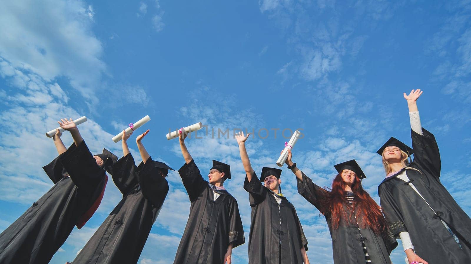 Cheerful graduates pose with raised diplomas on a sunny day