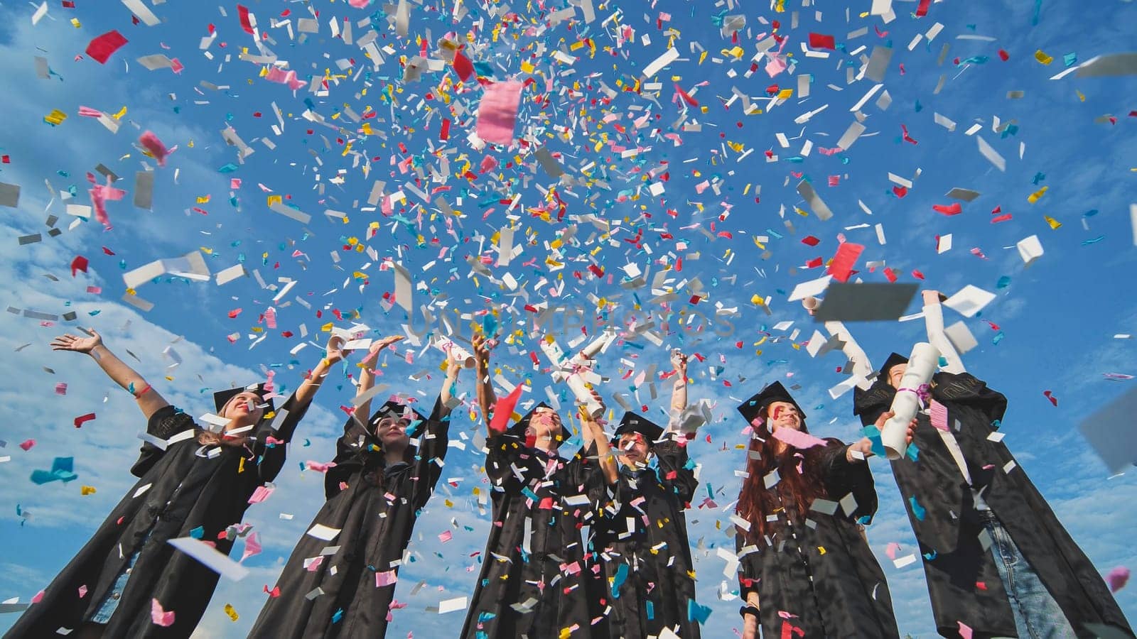 Happy graduates throw colorful confetti against a blue sky