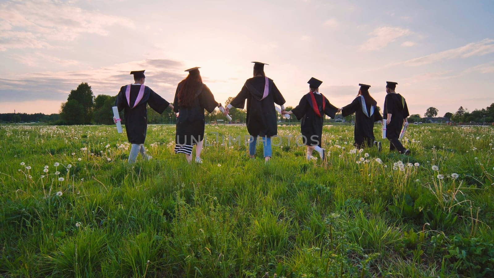 Six graduates in robes walk against the backdrop of the sunset. by DovidPro