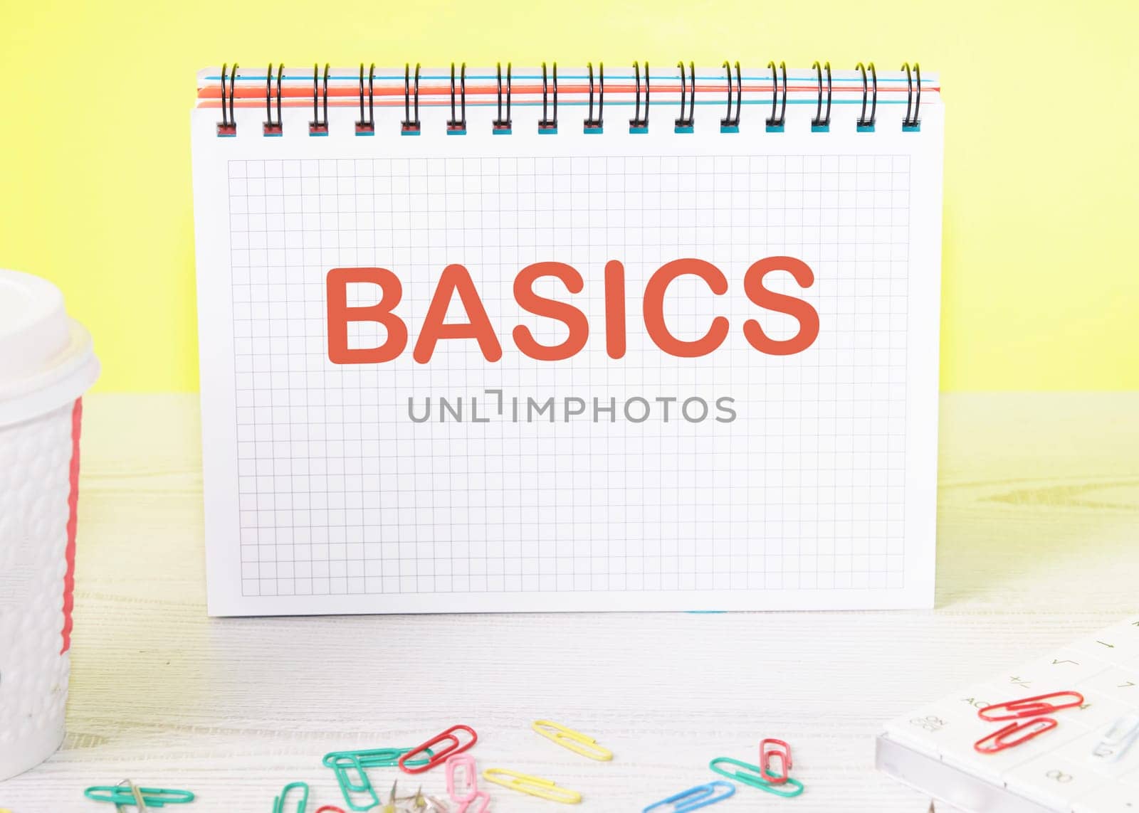BASICS the word is written on a blank sheet in a notebook standing on a table on a yellow background