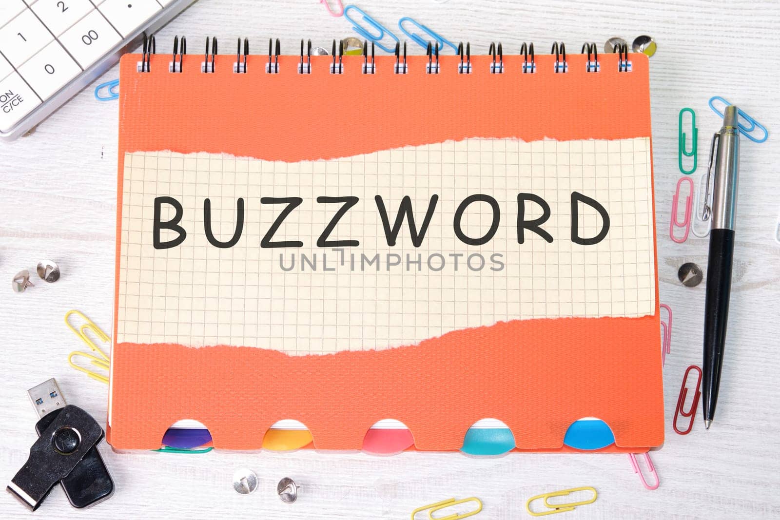 Buzzword word is written on a sheet in a cage lying on a notebook on the table next to stationery