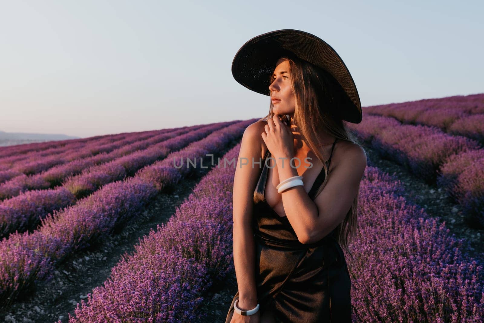 Woman lavender field. Happy carefree woman in black dress and hat with large brim walking in a lavender field during sunset. Perfect for inspirational and warm concepts in travel and wanderlust. by panophotograph