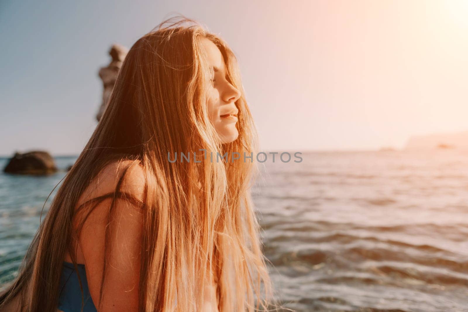 Close up shot of happy young caucasian woman looking at camera and smiling. Cute woman portrait in bikini posing on a volcanic rock high above the sea