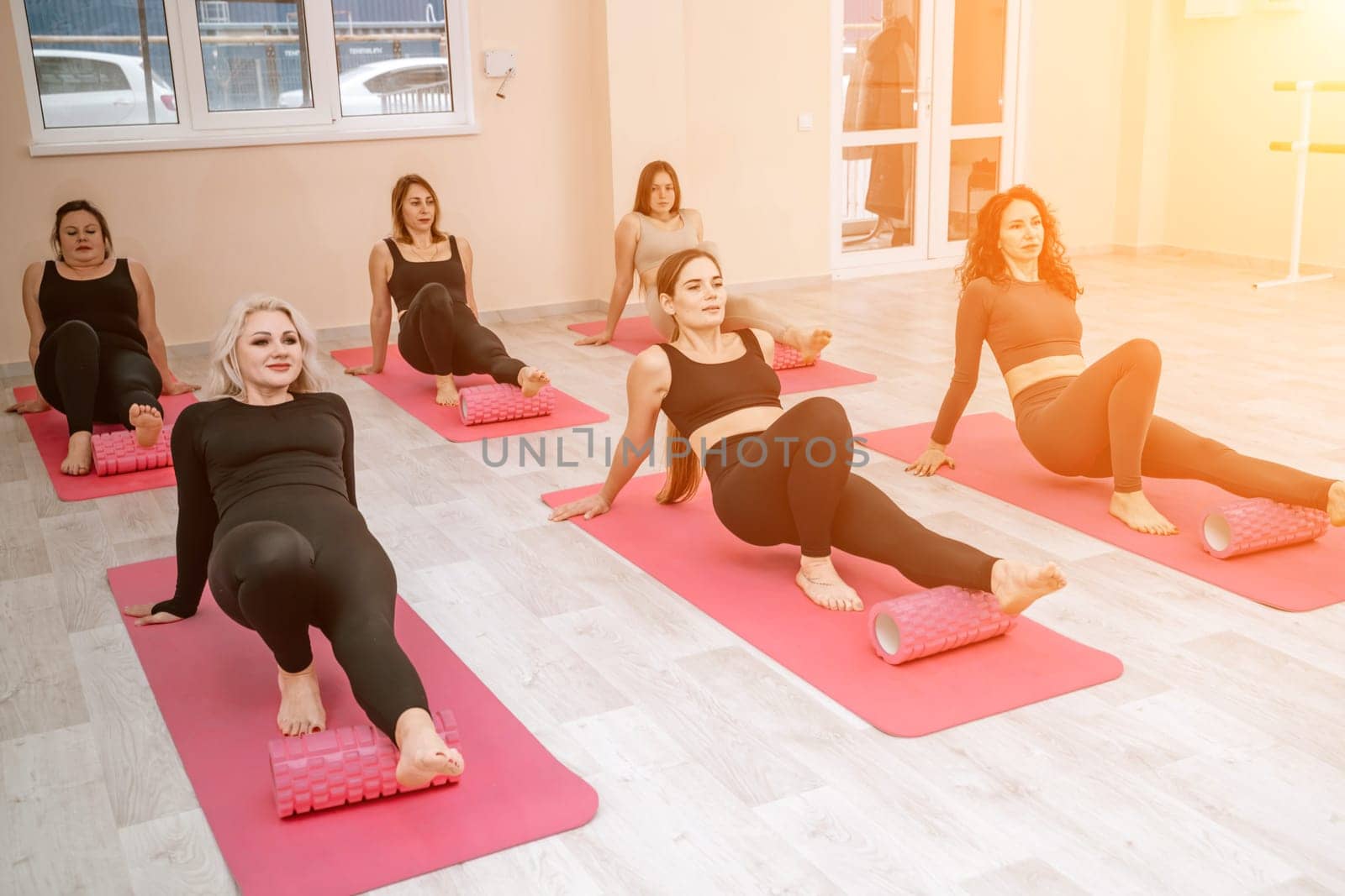 Athletic women doing fascia exercises on the floor with a foam roller massage tool to relieve back tension and relieve muscle pain. The concept of physiotherapy and stretching training by Matiunina