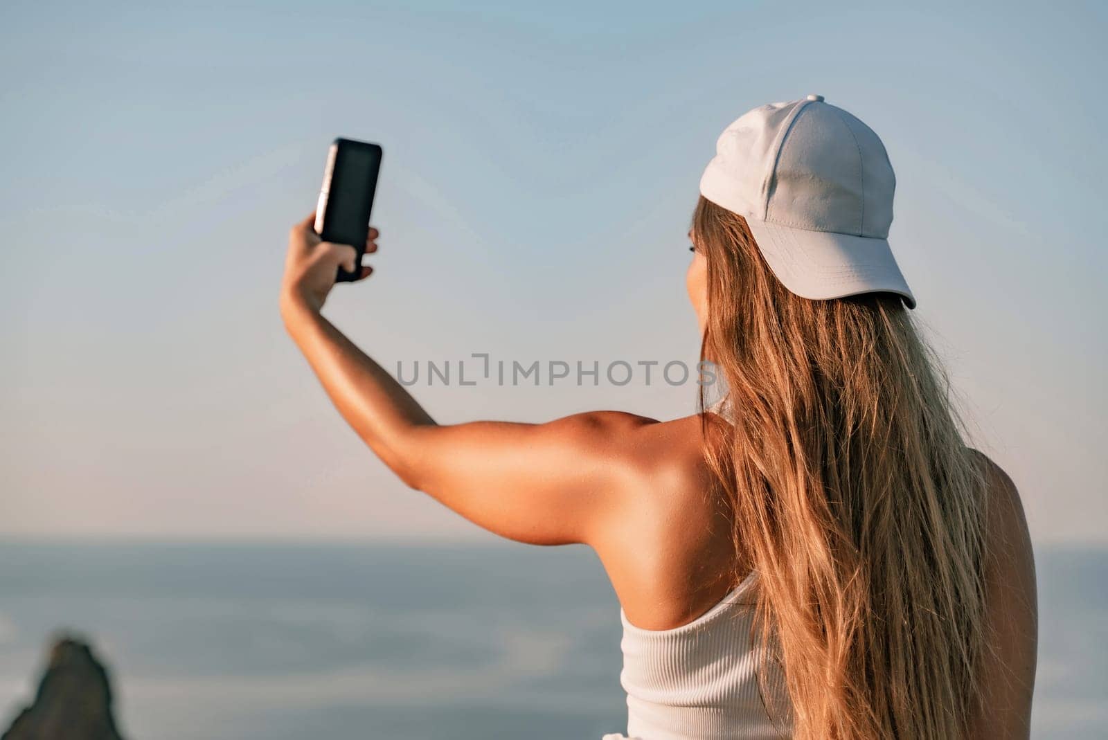 Selfie woman in cap and tank top making selfie shot mobile phone post photo social network outdoors on sea background beach people vacation lifestyle travel concept. by Matiunina