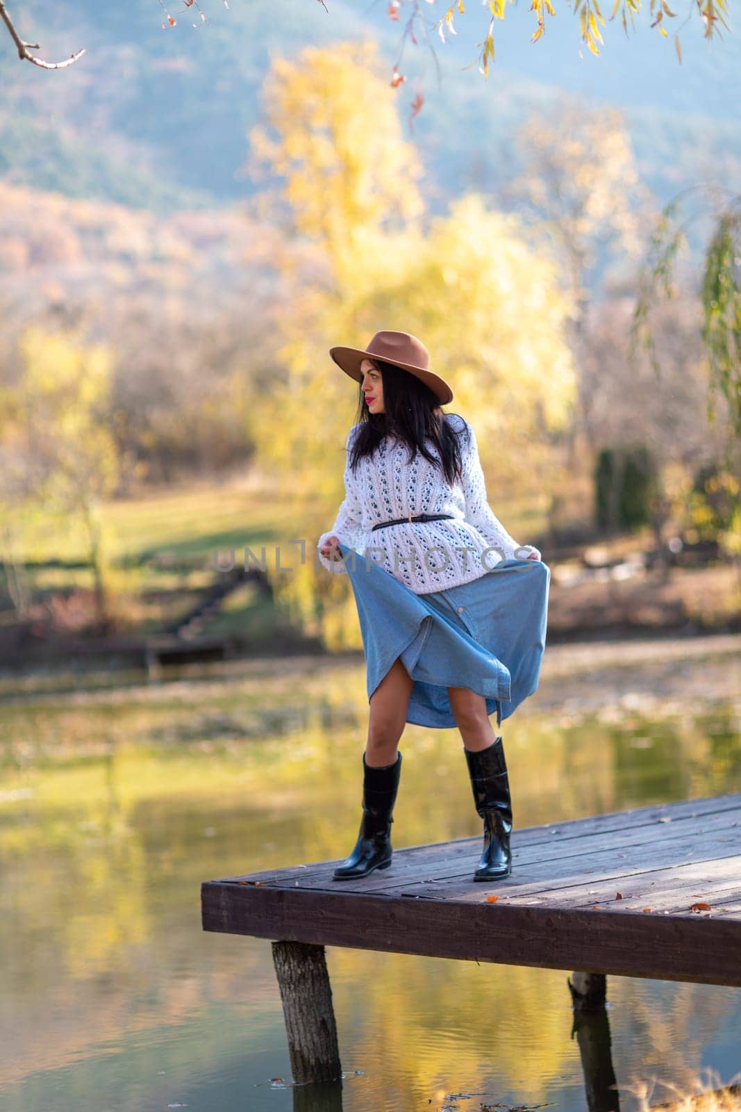 Autumn lake woman. She stands by a pond on a wooden pier in autumn and admires nature. The concept of tourism, weekends outside the city. by Matiunina