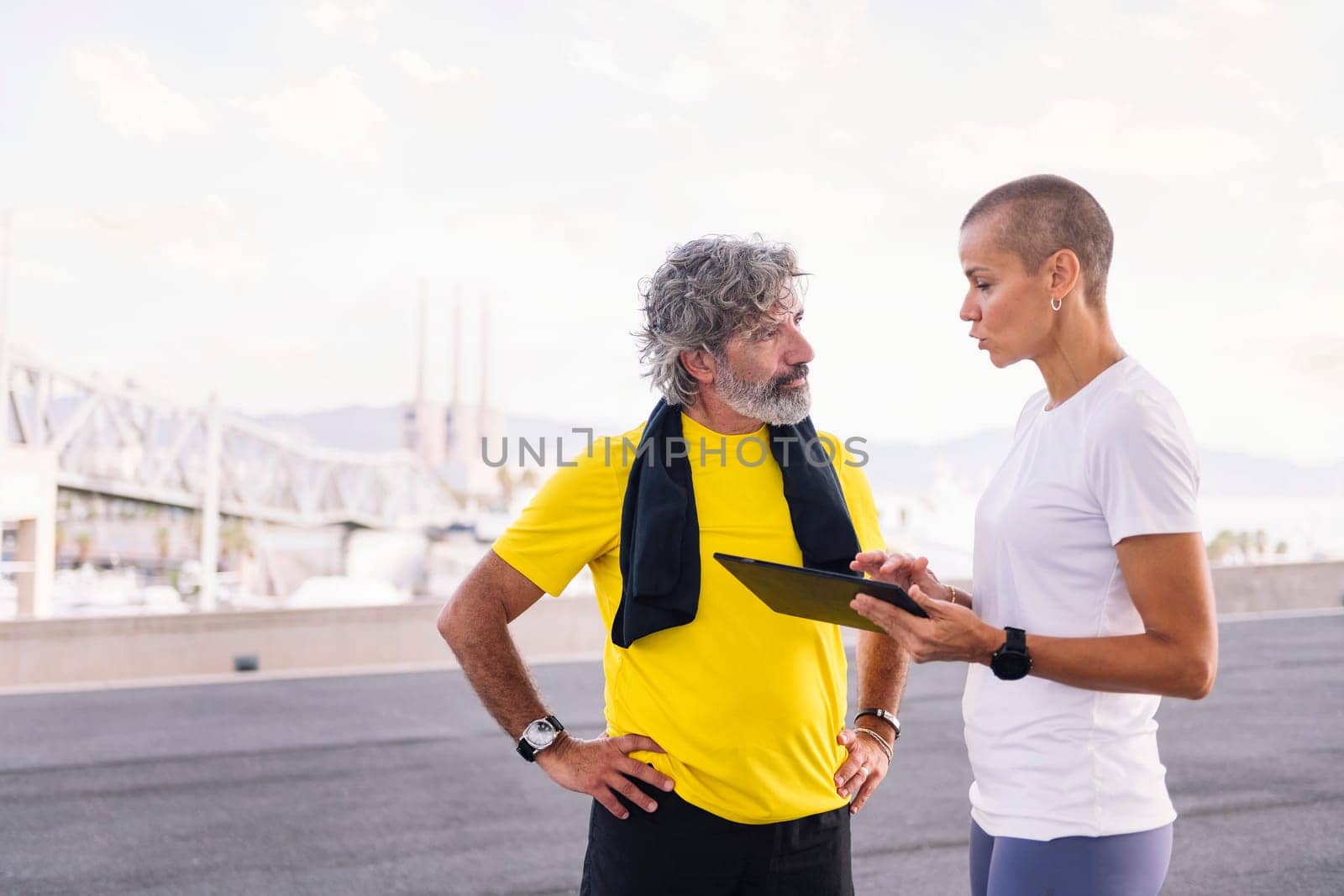 female personal trainer explaining workout with tablet to an elderly sports man, concept of active and healthy lifestyle in middle age, copy space for text