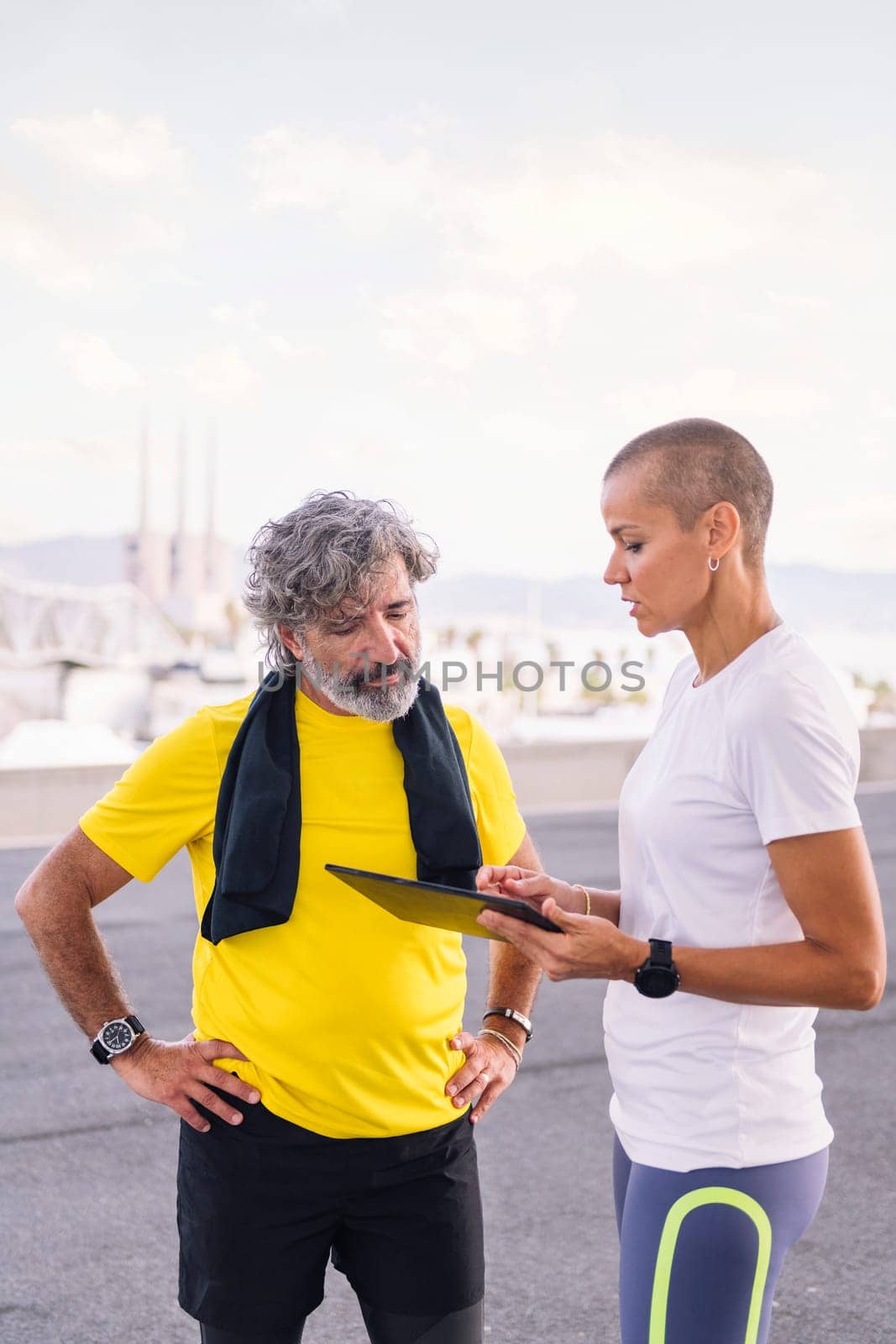 female personal trainer explaining workout with tablet to an elderly sports man, concept of active and healthy lifestyle in middle age, copy space for text