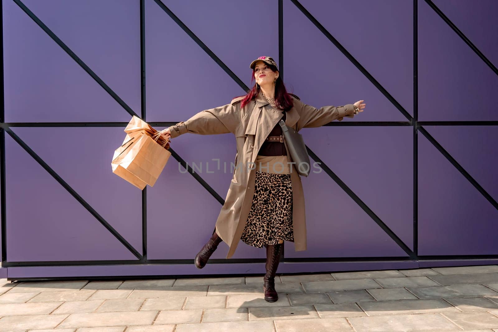 A happy shopaholic girl keeps her bags near the shopping center. A woman near the store is happy with her purchases, holding bags. Dressed in a leopard print dress. Consumer concept