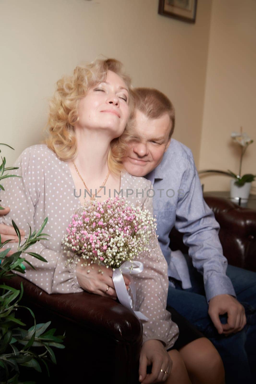 Loving adult couple communicates and embraces privately in the living room or in hotel. Woman is wearing business formal suit and man is wearing jeans and a shirt, indicating a close relationship