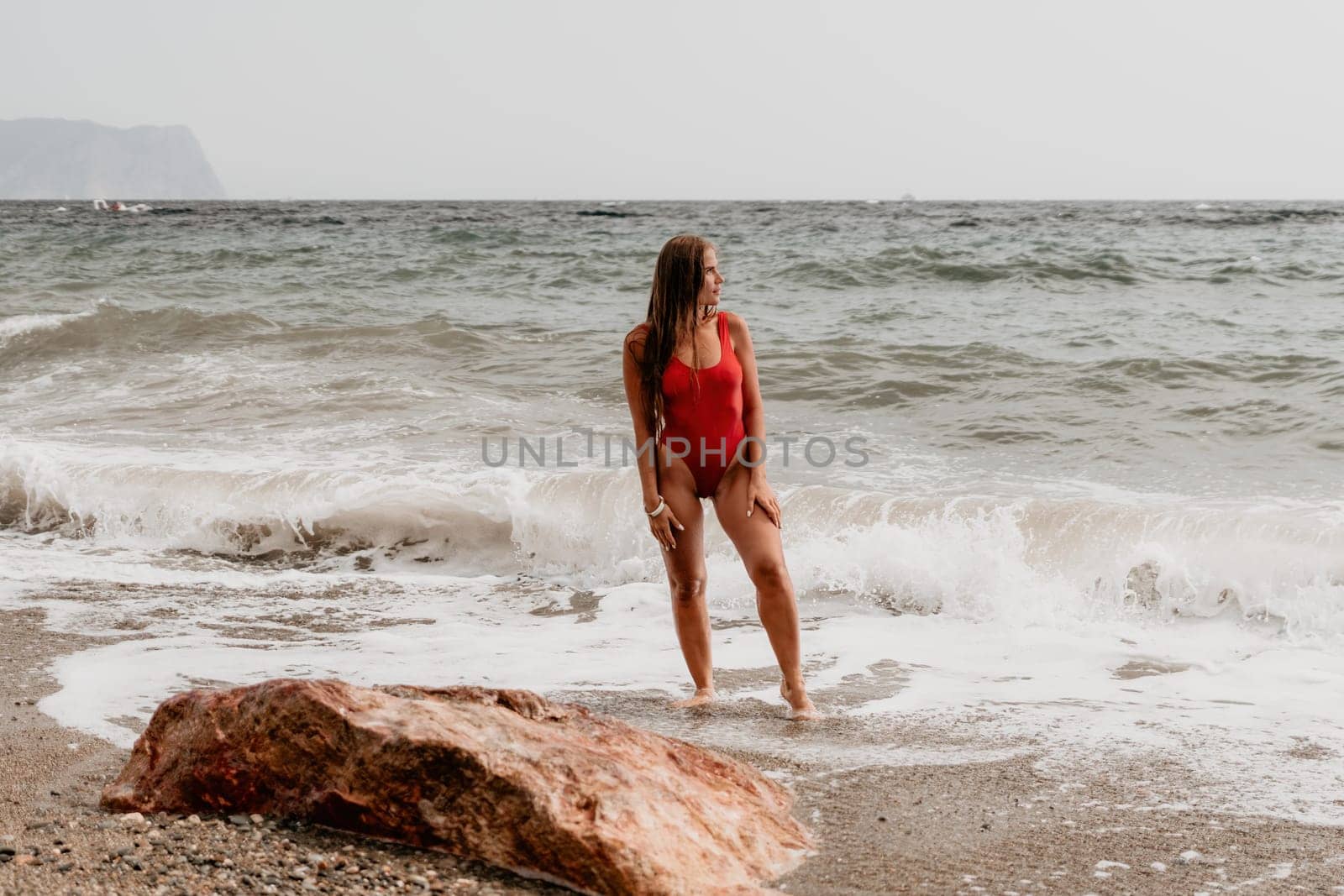 Woman summer travel sea. Happy tourist in red bikini enjoy taking picture outdoors for memories. Woman traveler posing on beach at sea surrounded by volcanic mountains, sharing travel adventure joy by panophotograph