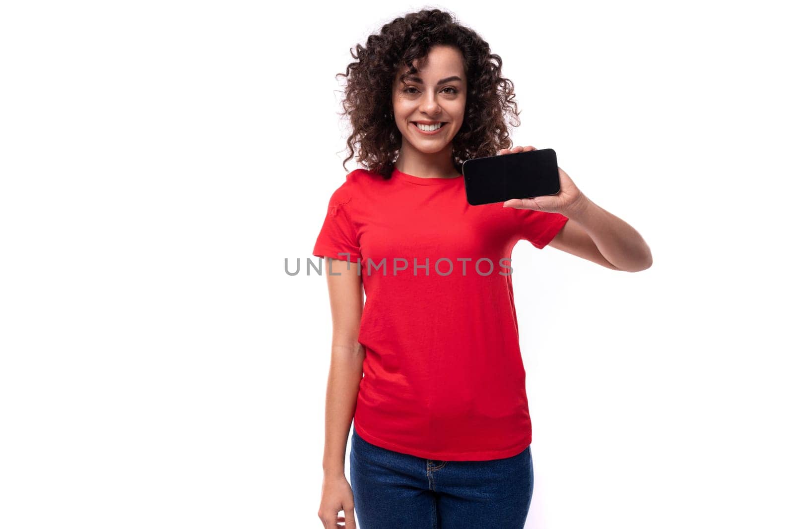 young active curly brunette woman dressed in a casual basic red t-shirt showing the screen of a mobile phone by TRMK