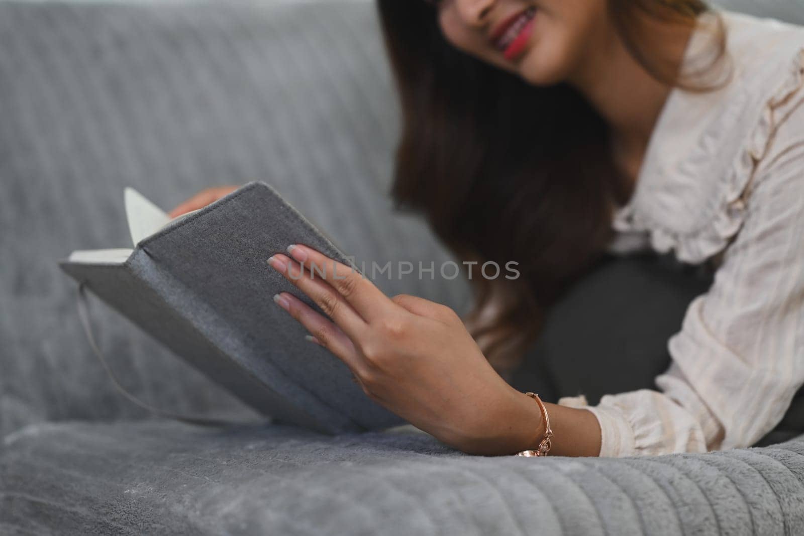 Carefree asian woman lying on couch and reading book. People, leisure and lifestyle concept.