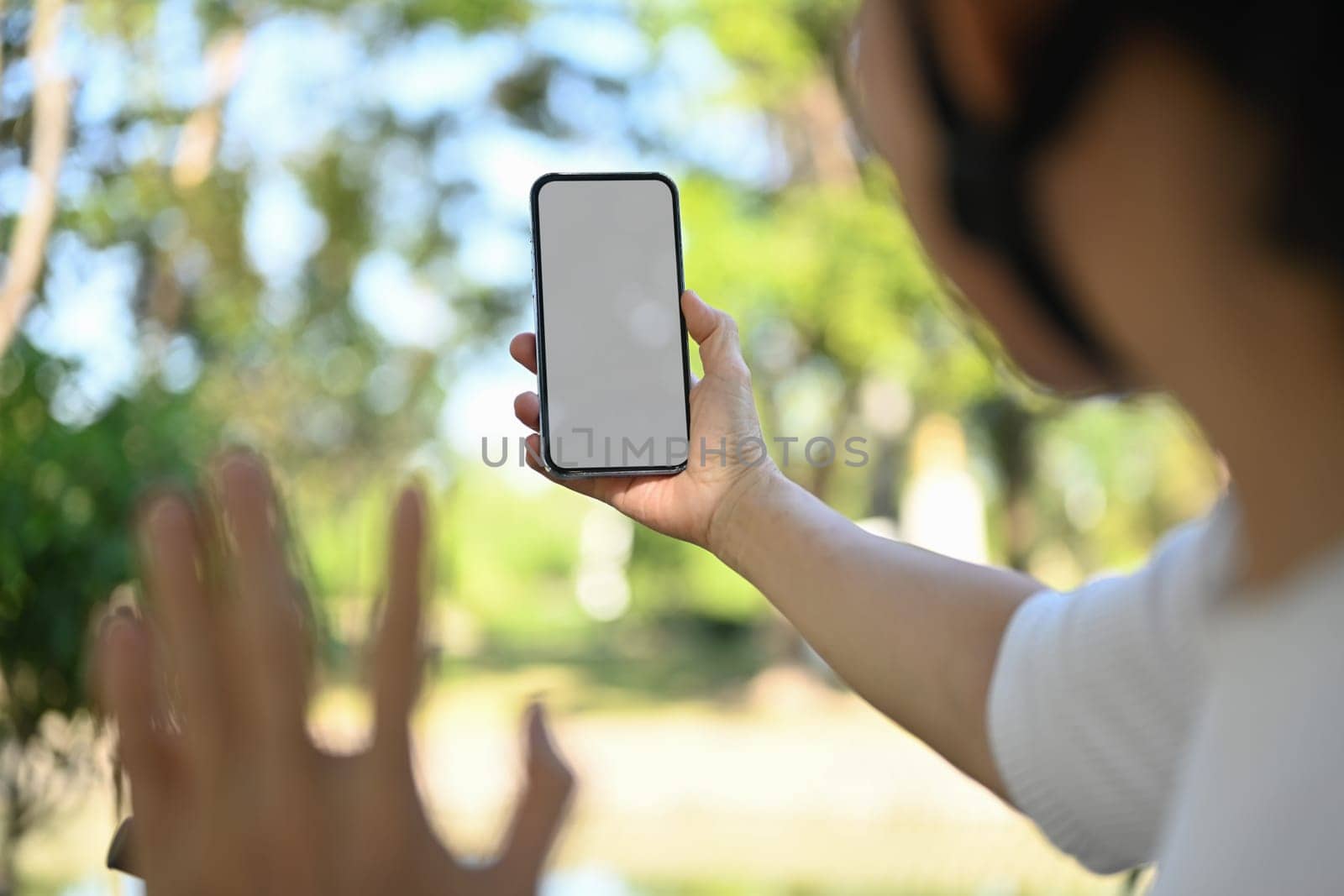 Active senior woman making video call with mobile phone while riding bicycle at the park.