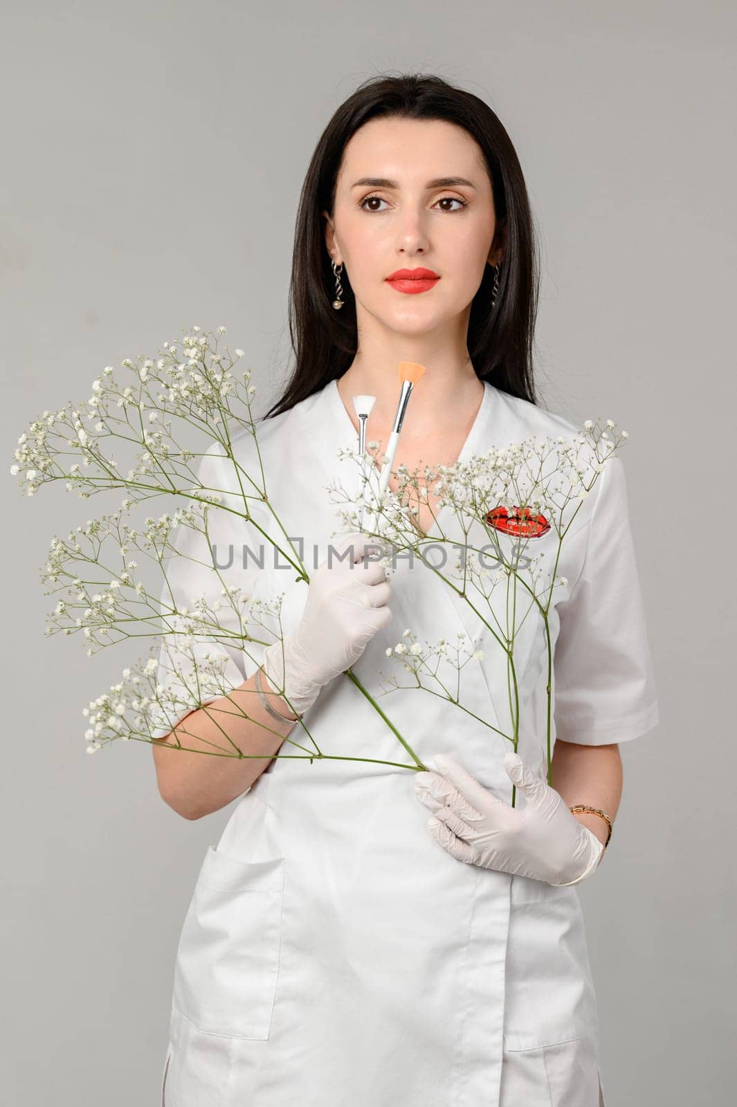 the girl holds two brushes in her hands on a white background, the girl is a beautician in white disposable gloves.