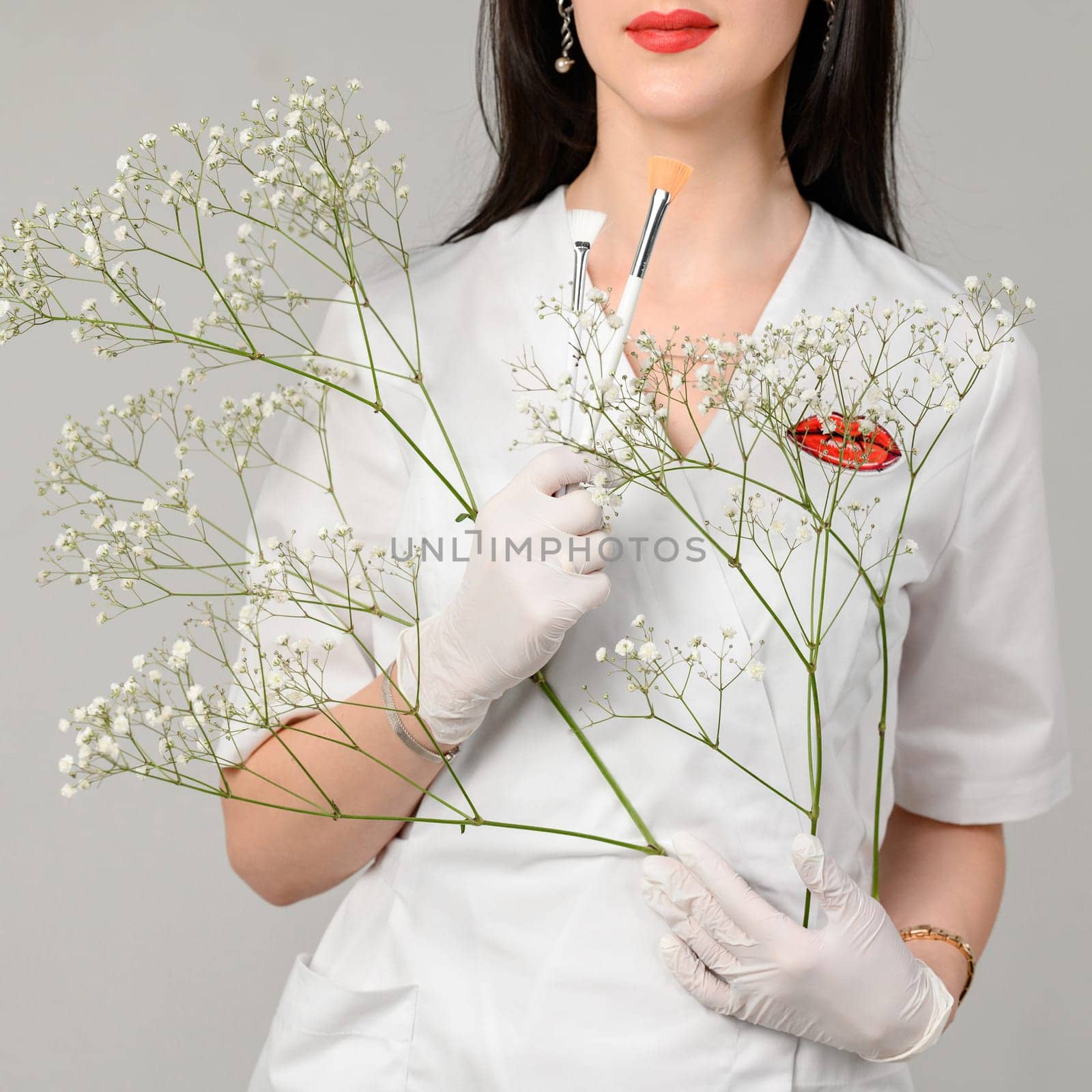 the doctor cosmetologist holds two brushes in her hands on a white background, the girl is a beautician in white disposable gloves.