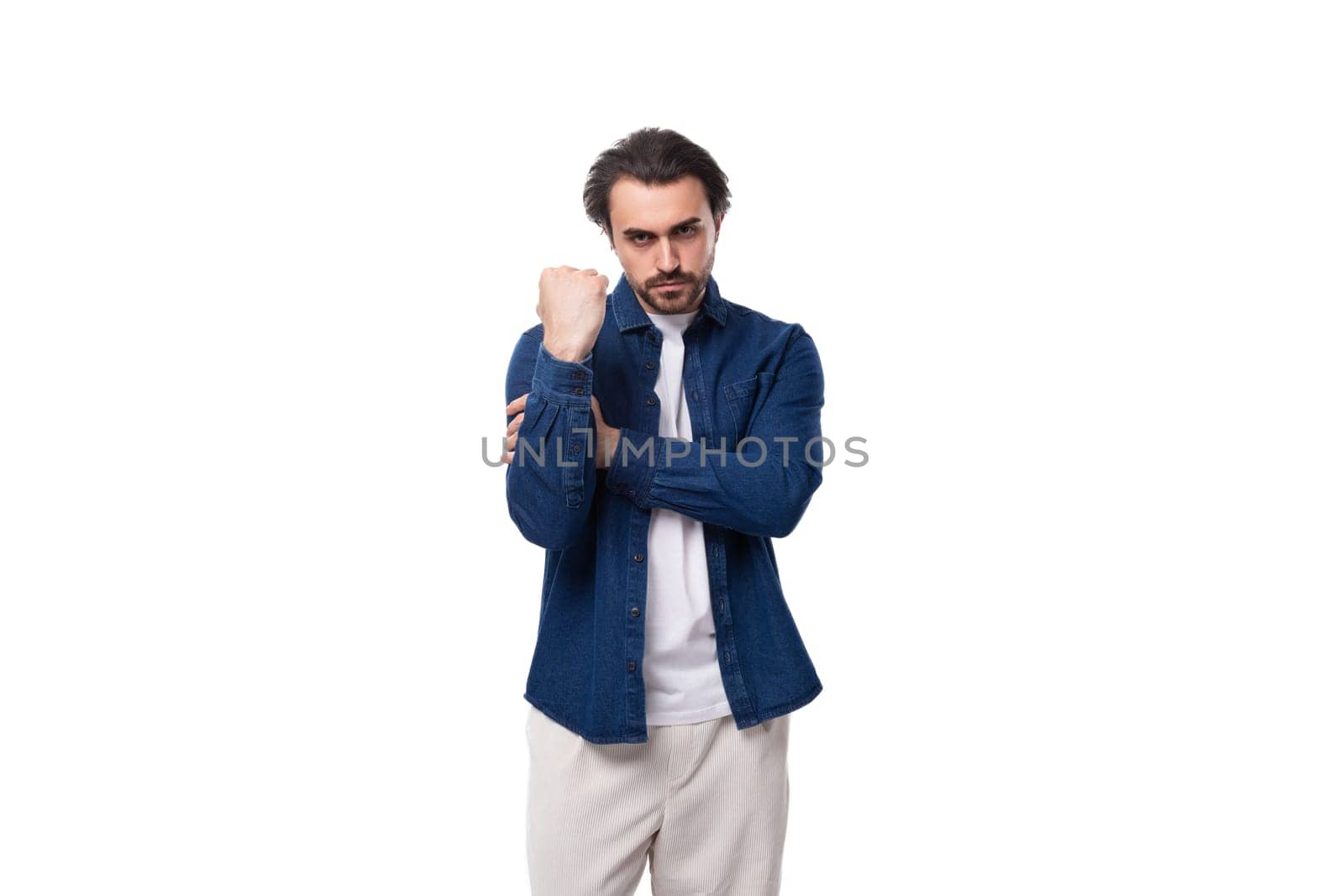 young serious handsome brutal brunette guy in a denim shirt and light-colored trousers by TRMK