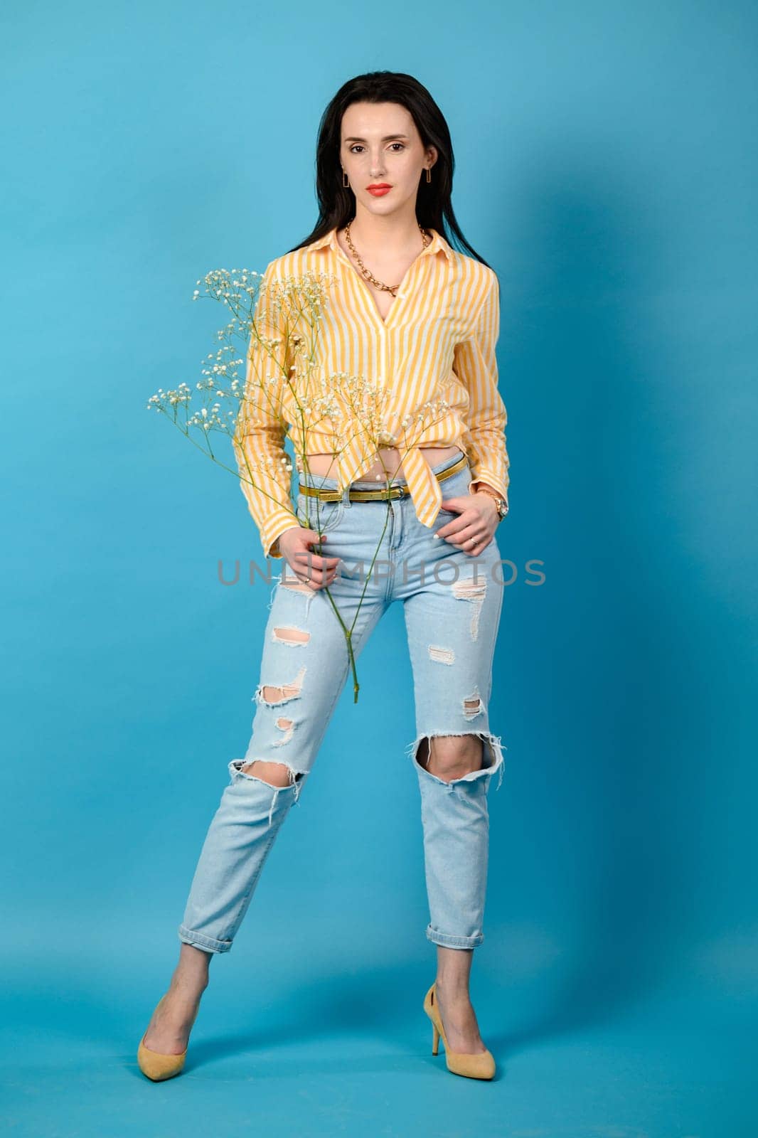 Brunette girl on blue background in blue jeans and yellow shirt, brunette girl with long hair, copy space.