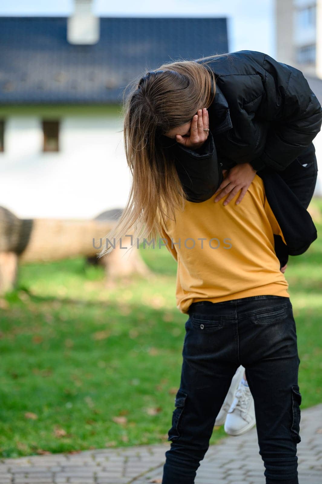 A young man carries a girl on one shoulder, youthful mischief in the park, a walk in the park.