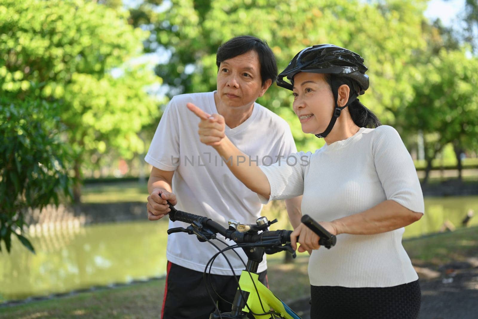 Beautiful senior couple taking a walk with bike in the park. Retirement activity and wellness concept. by prathanchorruangsak