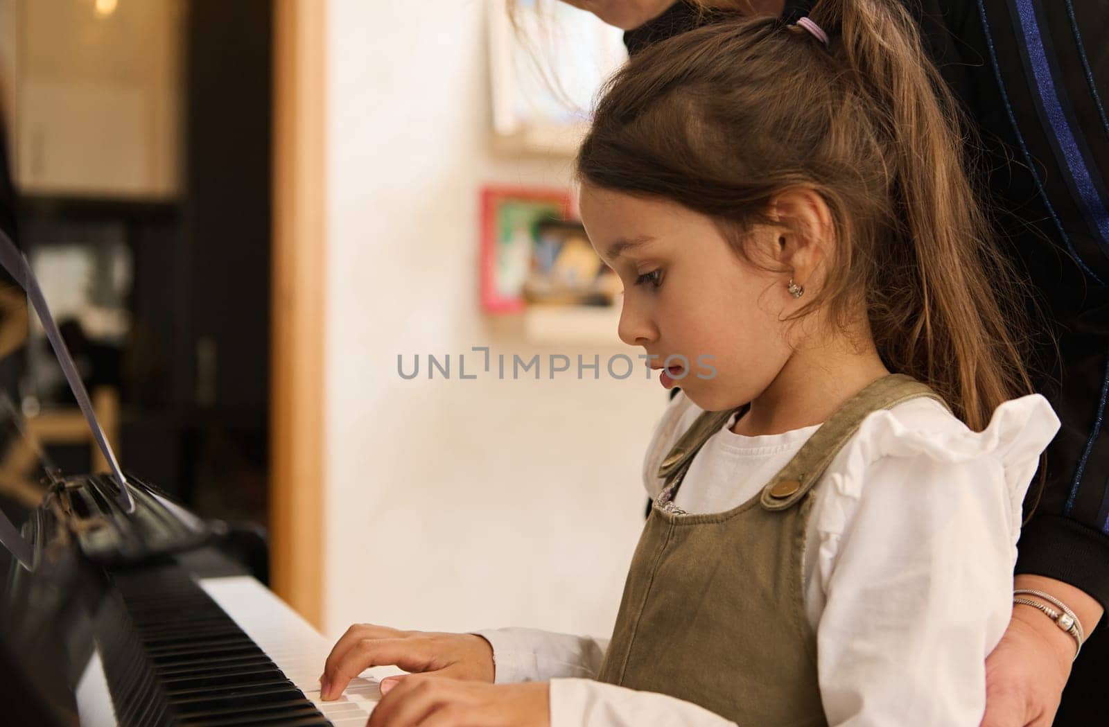 Adorable Caucasian little child girl playing piano under the guidance of her teacher. by artgf