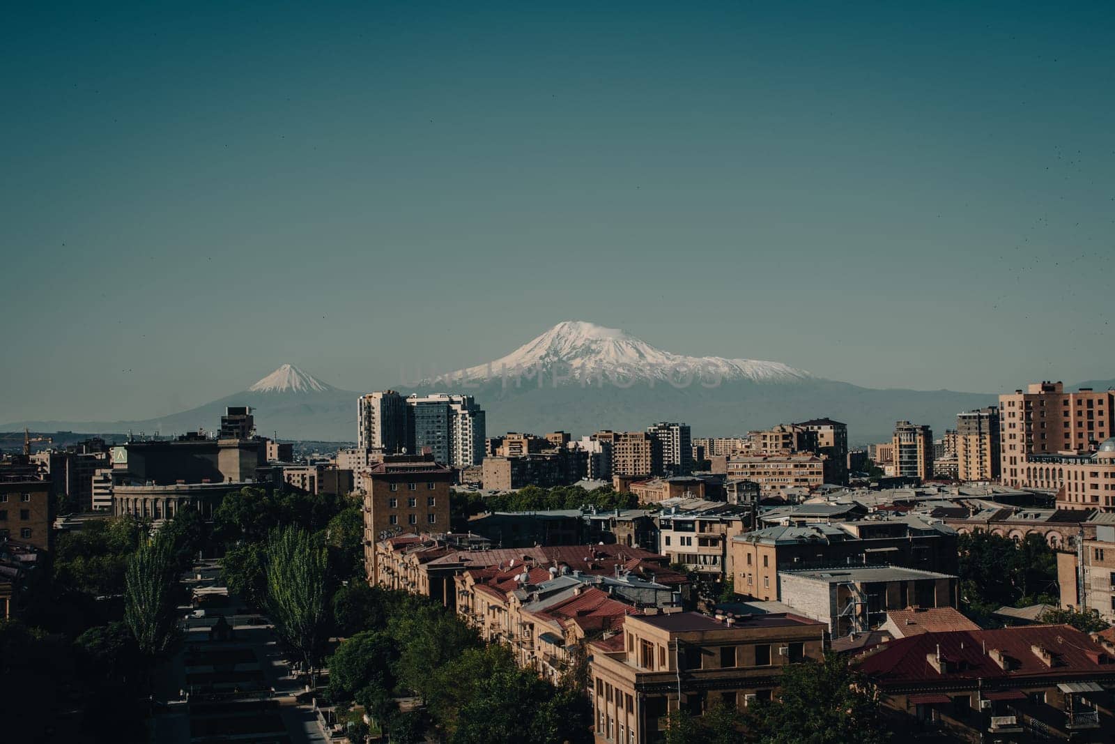 Cityscape with mountain view in a day time concept photo. Yerevan, capital of Armenia in front of mountain Ararat. Beautiful urban scenery from parkland. High quality picture for magazine, article