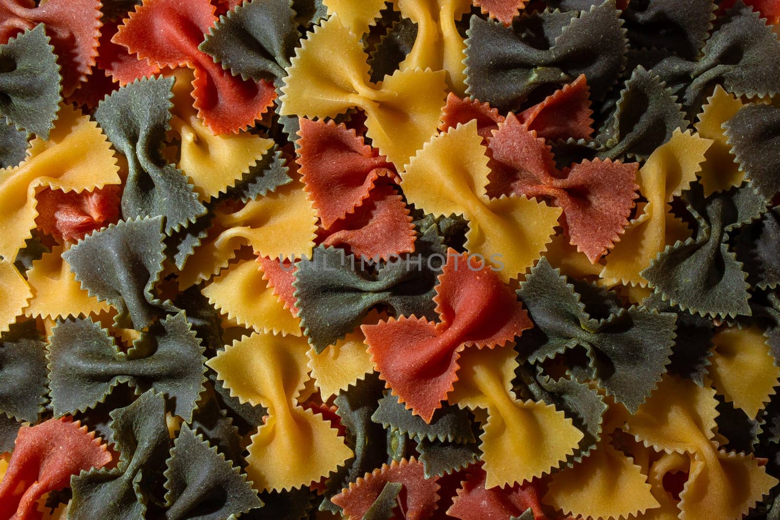 Uncooked Vibrant Colored Farfalle Pasta: A Culinary Canvas of Multicolored Bow-Tie Macaroni, Creating a Lively and Textured Background for Gourmet Cooking Enthusiasts. Colored Dry Pasta. Raw Macaroni