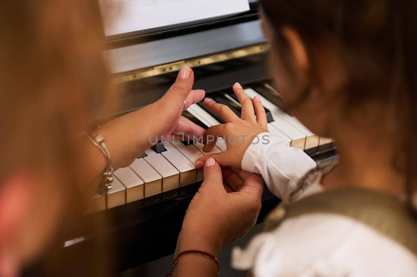 Kid girl learns playing grand piano, touches piano keys under the guidance of her teacher during individual music lesson by artgf