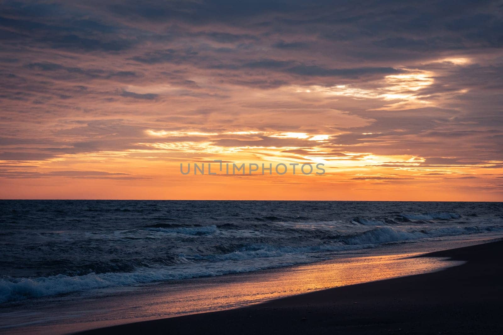 Wet surfline of black beach landscape photo. Beautiful nature scenery photography with bright sky on background. Idyllic sunset scene. High quality picture for wallpaper, travel blog, magazine, article